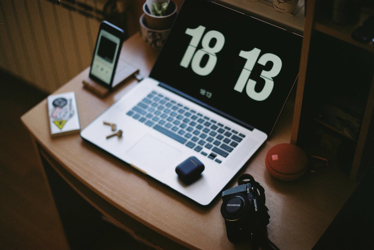 A cozy home workspace with a laptop, smartphone, camera, and headphones. Ideal for tech enthusiasts.